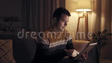 深夜坐在沙发上用数码平板电脑在家工作的微笑男人的肖像