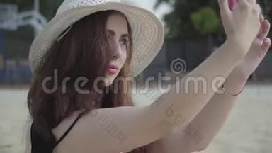 可爱的年轻女人在夏<strong>天</strong>的白色帽子自拍她的手机休息在海滩上。 <strong>夏季</strong>休闲概念