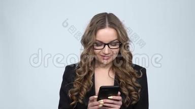 一个微笑的年轻女子在<strong>录音</strong>室里用灰色背景的手机发短信，动作很慢
