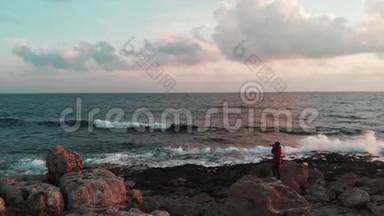 一位年轻的白种人女<strong>摄影</strong>师正站在岩石海岸的大<strong>石头</strong>上拍摄美丽的粉红色照片