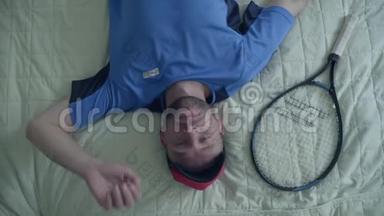 在旅馆里，穿着<strong>运动器材</strong>的英俊疲惫的网球运动员正拿着网球拍躺在床上。积极的生活方式