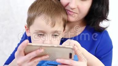 一个女人抱着一个小男孩拥抱他。 孩子触摸手机的触摸屏，在一个游戏中玩孩子的游戏