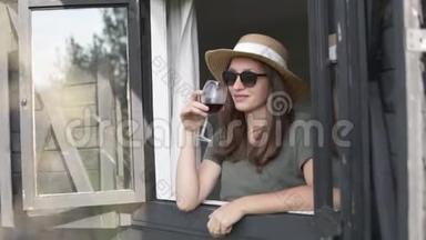 一个戴帽子的女人拿着一杯红酒<strong>看</strong>着<strong>窗外</strong>
