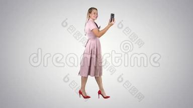 粉红女郎手持智能手机录制视频博客，在渐变背景下行走。