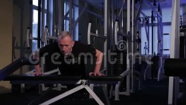 一位老人在健身房把自己从长凳上推下来。复制空间。
