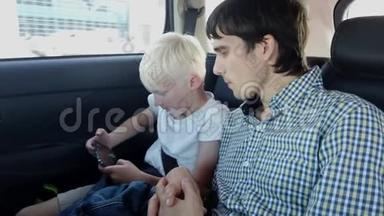 帅气的父亲带着儿子坐在汽车座椅上，一边玩智能手机一边在后座<strong>坐车</strong>
