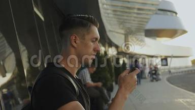 迷人的年轻人穿着黑色t恤使用他的智能手机，<strong>录音</strong>和滚动。 在机场或汽车站。