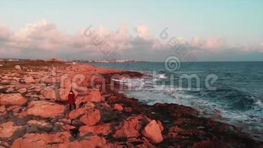 年轻的女摄影师站在岩石海岸，在日落时拍摄美丽的海浪
