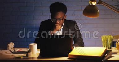 办公室工作人员在深夜工作在笔记本电脑上。 他打哈欠，喝咖啡。 只有一个商人