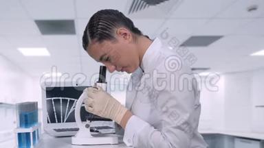 一位女实验室技术人员坐在化学实验室笔记本电脑旁的桌子旁，在一个实验室里看生物样本