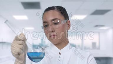 一位女<strong>实验室</strong>技术人员在玻璃瓶中检查一种<strong>蓝色</strong>液体，并在一个科学<strong>实验室</strong>进行临床研究。 关闭