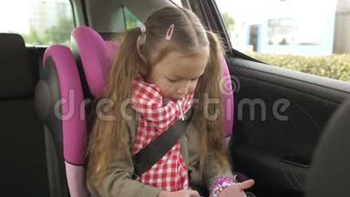 小女孩在车里用智能手机。 可爱的少女在智能手机上玩，而骑在后座上开车