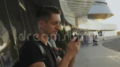迷人的年轻人穿着黑色t恤使用他的智能手机，录音和滚动。 在机场或汽车站。