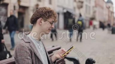 戴眼镜和夹克的年轻嬉皮士的侧视使用他的智能手机，在屏幕上滚动，一边微笑