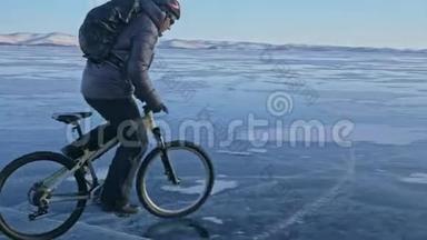 人在冰上骑自行车。 骑自行车的人穿着灰色<strong>羽绒服</strong>，背包和头盔。 冰冻的冰