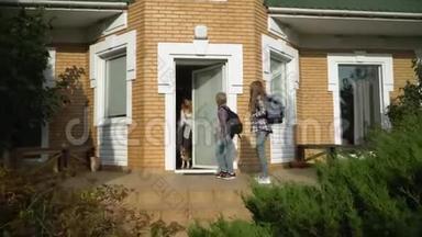小可爱的男孩和女孩带着背包离开家去上学。 微笑的妈妈挥手。 快乐的爱