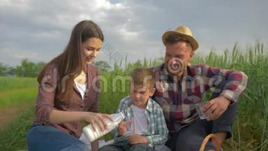 农村家庭，幸福的女人在大自然的粮田野餐中给儿子和丈夫倒牛奶