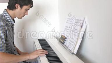英俊的人试着弹钢琴。 年轻人用手机学弹钢琴