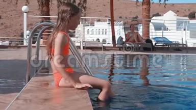 在<strong>度假酒店</strong>里，坐在池边的少女用双腿蘸水。 小女孩在游泳池旁泼水