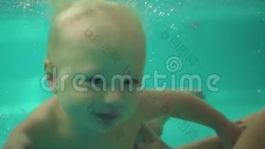 可爱的金发幼儿正在游泳池的水下游泳，直到他的母亲帮助他出去。 一个