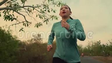 慢速跟踪万向节拍摄年轻健康的亚裔韩国妇女在日落时分在树林中跑步做慢跑锻炼
