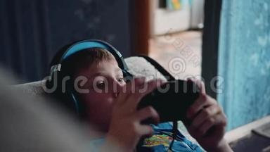 这个男孩在沙发上玩电子游戏，头上戴着耳机。 特写足够了。 多媒体娱乐。