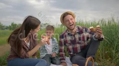 快乐的家庭<strong>周</strong>末，快乐的男人一边给女人喂面包，一边和孩子一起在<strong>绿色</strong>的田野里喝牛奶放松野餐