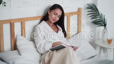穿着<strong>白色浴袍</strong>的年轻美女躺在床上看书