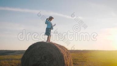 日落时干草跳跃的小女孩。 在乡下的干草堆附近的女孩。