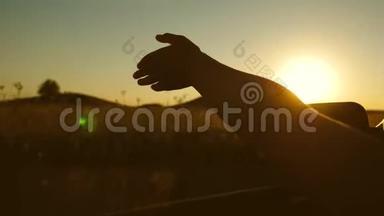 女孩`手挥动太阳。 <strong>乘车</strong>旅行。 司机的手正在玩太阳从车窗对着美丽的日落。