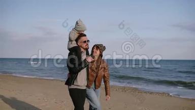 一个<strong>年轻时</strong>尚的戴墨镜的父亲把他的儿子扛在肩上，一个<strong>年轻</strong>的家庭在海边散步，享受关节