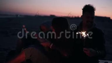快乐的，微笑的<strong>三口之家</strong>在海滩上坐在篝火旁，带着火花拥抱，烤着