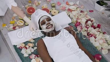 美丽的年轻非洲妇女在温泉度假胜地休息放松，而美容学家在她的脸上涂了面膜。 健康