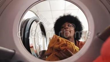 年轻的非洲裔美国妇女把脏衣服装进洗衣机。 洗衣服。 从里面看。