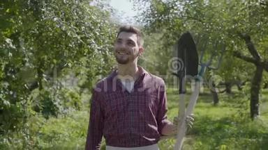 年轻的笑着留着胡子的农民手里拿着铲子和草叉穿过花园。 <strong>农村生活</strong>观念