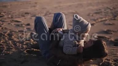 快乐，年轻的妈妈穿着秋装躺在沙滩上，快乐地拥抱着她的孩子，把她抱起来