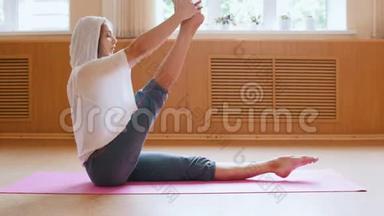 年轻苗条的女人坐在瑜伽垫上做腿部练习-舞蹈室