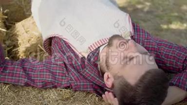 大胡子的年轻人躺在干草上吃新鲜的苹果。 农夫下班后休息。 乡村生活方式，乡村风格..