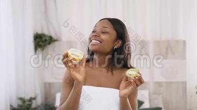 滑稽有趣的非裔美国年轻女子的肖像镜头，她<strong>手中</strong>拿着猕猴桃和橙色的一半，<strong>手中</strong>拿着光