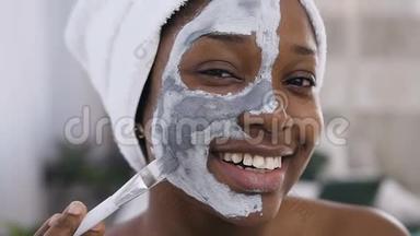微笑的美国黑人女孩的特写镜头，头上用毛巾敷面膜，化妆