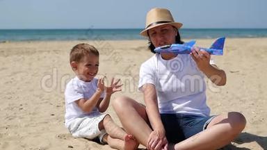 快乐的母亲和儿子在阳光明媚的夏日坐在沙滩上玩玩具<strong>飞</strong>机