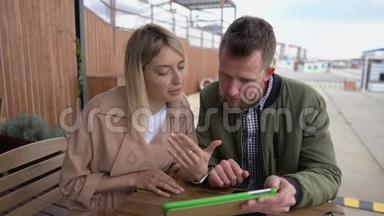 年轻夫妇正坐在户外的咖啡馆里通过平板电脑浏览互联网网站