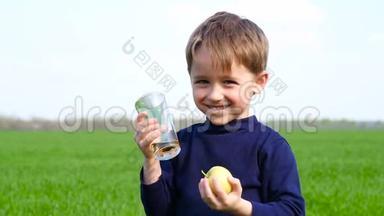 孩子拿着一个绿色的<strong>苹果</strong>和一杯<strong>苹果</strong>汁。 男孩在大自然的背景下喝<strong>果汁</strong>，笑。