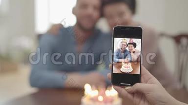 肖像女用手在手机上拍了一张照片，照片上的是快乐微笑的成熟女人和成年孙子拥抱在一起，两人都在
