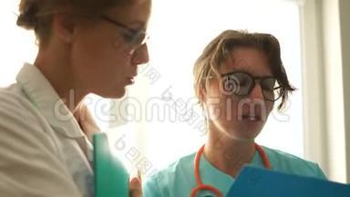 两名女医生在一个<strong>医院的</strong>房间里交谈，手里拿着笔记本，脸上写着笔记。 医疗和保健