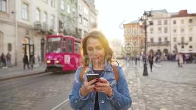 日落时分，女人用智能手机走在老街上。 有轨电车在后台。 交流、社会