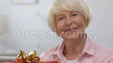带着红色礼品盒、微笑着看镜头的快乐老年妇女周年庆典