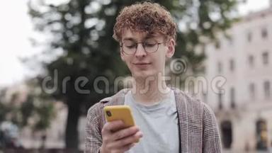 戴眼镜的年轻学生使用他的现代手机设备，在屏幕上滚动微笑行走户外