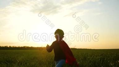 一个穿着超级英雄服装的快乐的孩子穿过绿草，在夕阳的背景下跑到镜头前