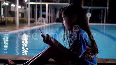 亚洲<strong>儿童</strong>女孩使用智能手机在<strong>游泳</strong>池附近放松。